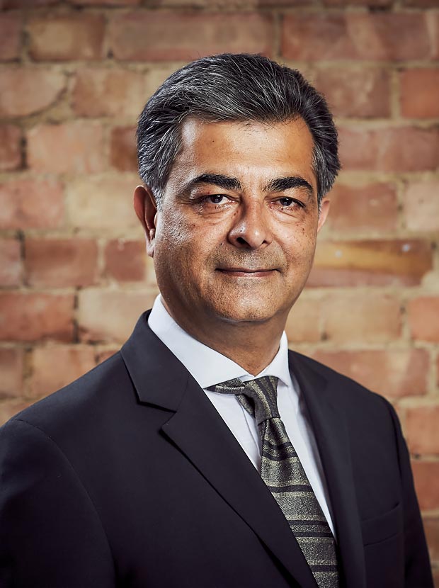 A colour head and shoulder photo of Minesh Sheta Chief Financial Officer at Westhill against a brick wall backdrop